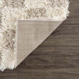 Close-up of the Atira Light Brown Checkered Area Rug showing shag texture, checkered pattern, and rug backing. Fold