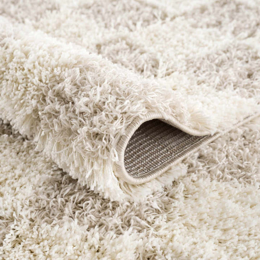 Close-up of the plush Atira Light Brown Checkered Area Rug, showing cream and light brown shag texture. Fold