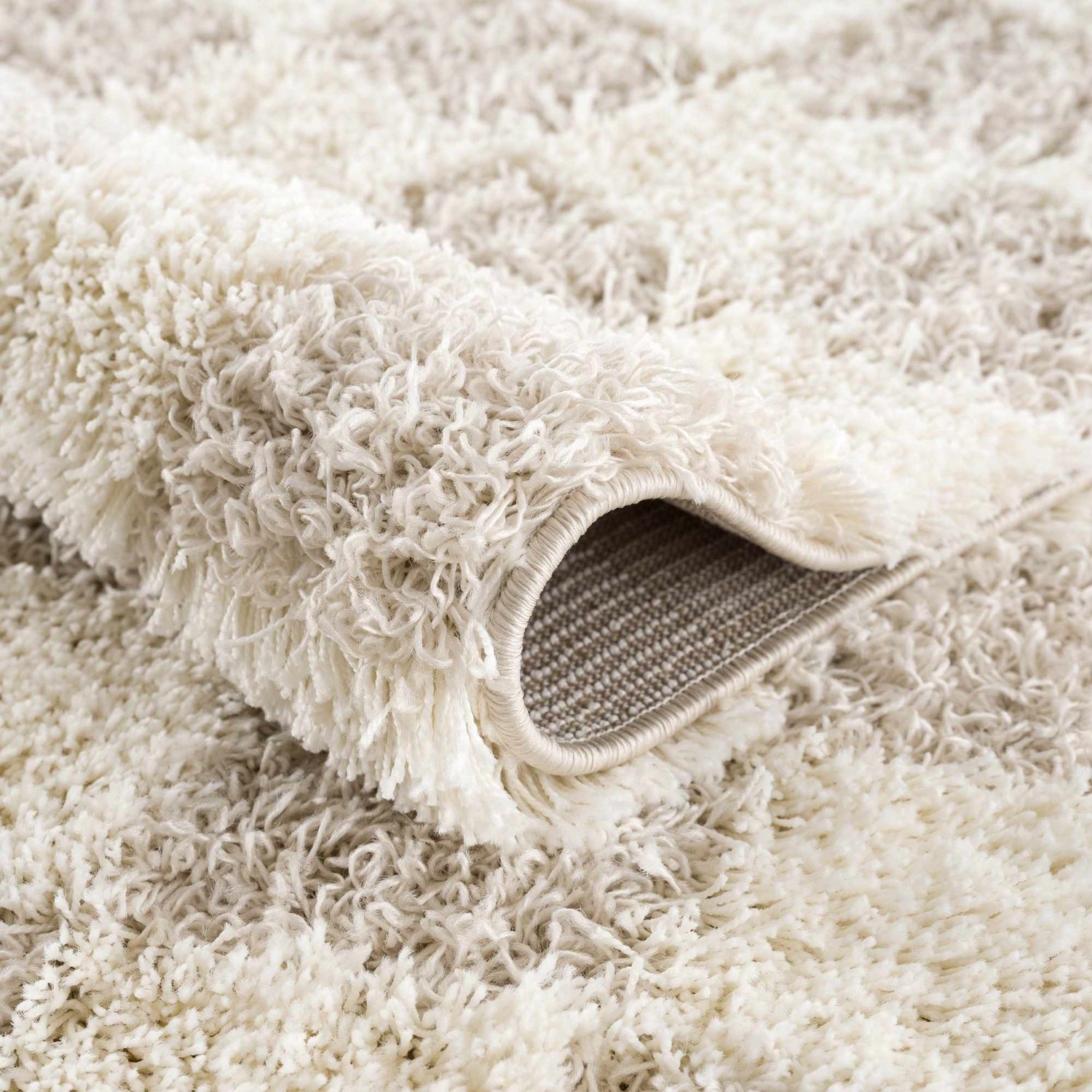 Close-up of the plush Atira Light Brown Checkered Area Rug, showing cream and light brown shag texture. Fold