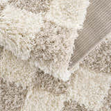 Close-up of the Atira Light Brown Checkered Area Rug showing its cream and light brown shag texture and woven backing. Fold