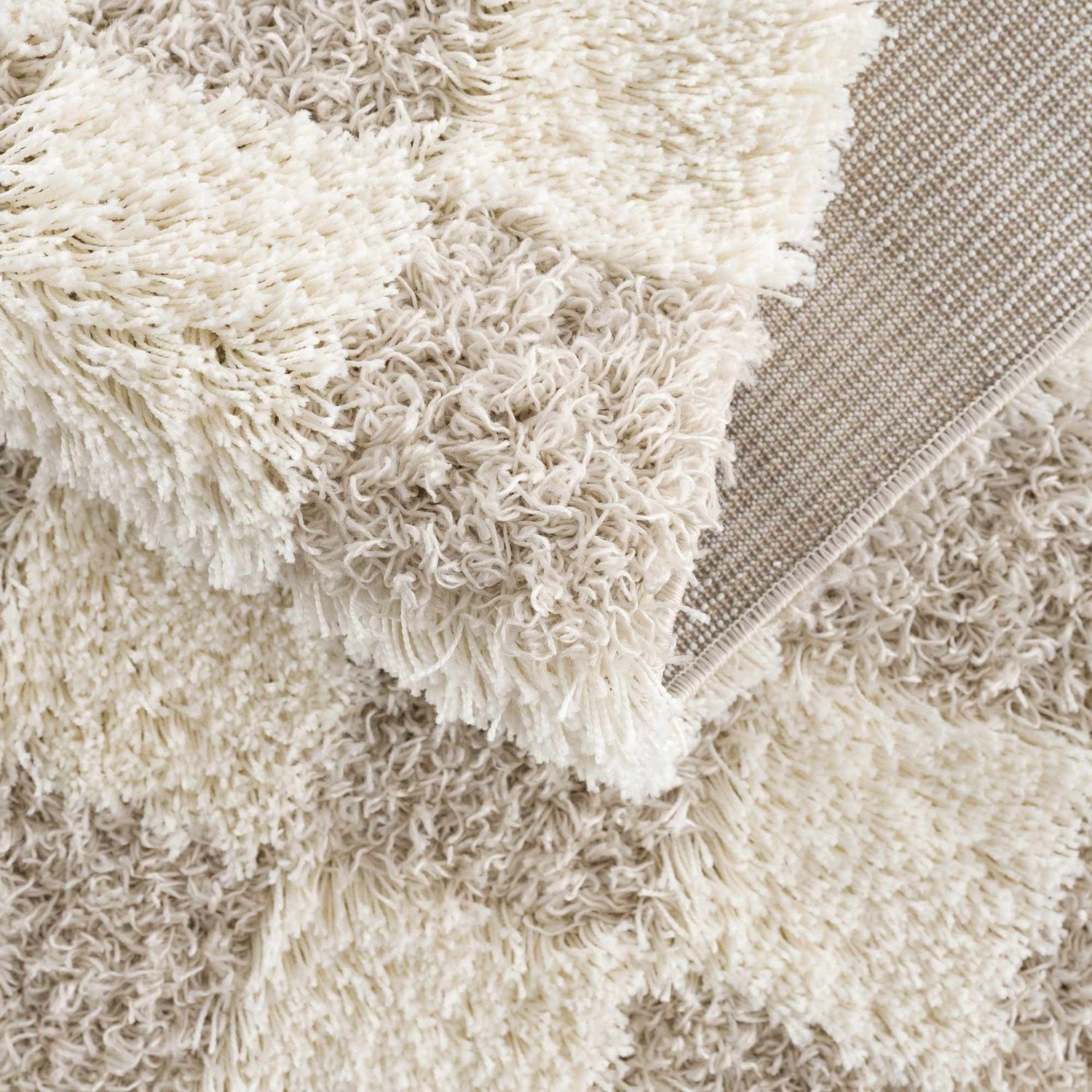 Close-up of the Atira Light Brown Checkered Area Rug showing its cream and light brown shag texture and woven backing. Fold