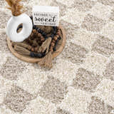 Close-up of the Atira Light Brown Checkered Area Rug, a shag rug with a cream and light brown geometric pattern. Roomscene-Rectangle