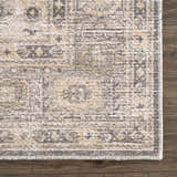 Close-up of the Keola Washable Area Rug. Farmhouse style rug with traditional pattern in beige, gray, and cream on wood floor. Swatch