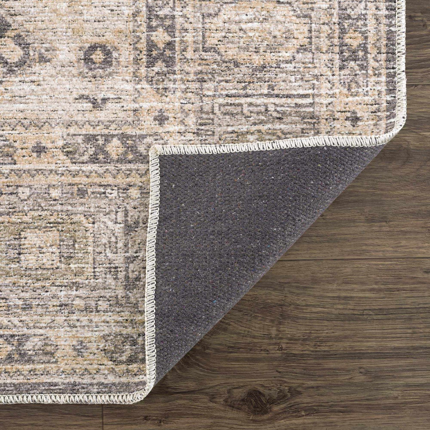 Close-up of the Keola Washable Area Rug showing a traditional design with beige, gray, and white tones and a dark gray backing. Fold