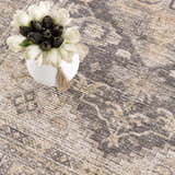 Close-up of the Keola Washable Area Rug featuring a traditional gray and beige pattern and a vase of black and white tulips. Styleshot