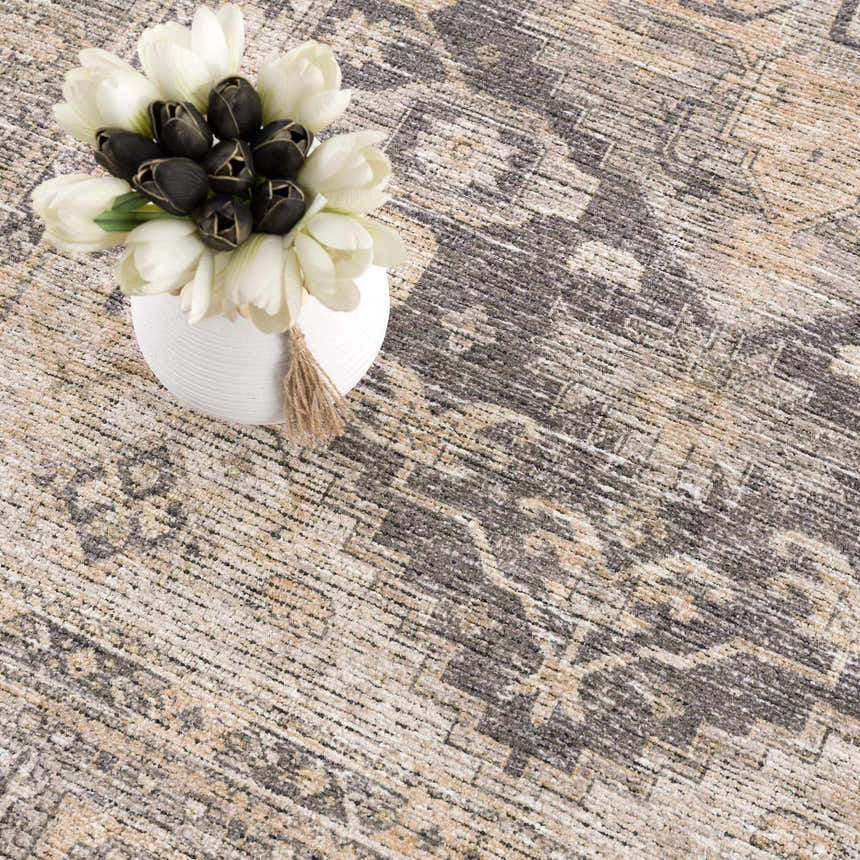 Close-up of the Keola Washable Area Rug featuring a traditional gray and beige pattern and a vase of black and white tulips. Styleshot