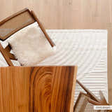 Top-down shot of the Deron White Washable 3D Rug styled with a wood table and chair on a light wood floor. Styleshot