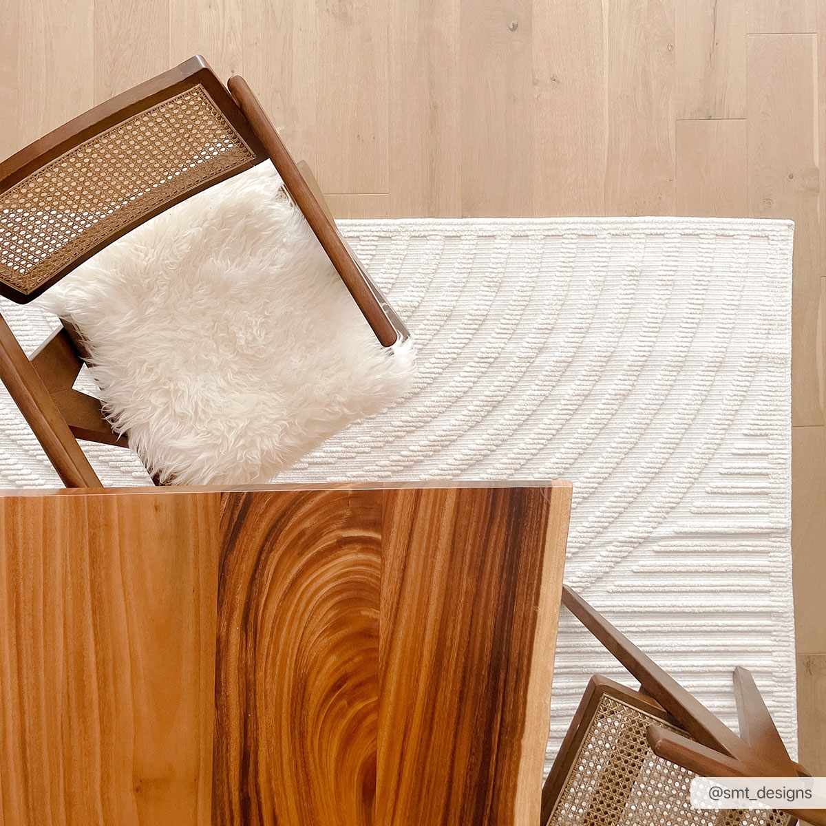 Top-down shot of the Deron White Washable 3D Rug styled with a wood table and chair on a light wood floor. Styleshot