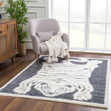 Living room scene with a Zane Charcoal Tibetan Tiger Plush Rug, gray chair, wood cabinet, and plant. Roomscene-Rectangle