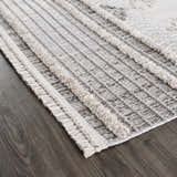 Close up of the Amaga High-Low Rustic Rug. Charcoal, cream, and gray geometric pattern with high-low texture and fringe detail. Corner