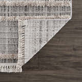 Close-up of the Amaga High-Low Rustic Rug showing texture, geometric pattern, fringe, and color palette of charcoal, cream, and gray. Fold