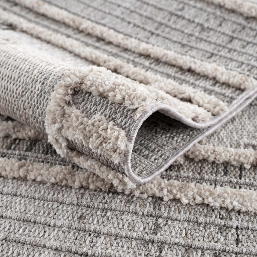 Close-up of the Amaga High-Low Rustic Rug, showing its charcoal, cream, and gray geometric pattern and textured, high-low pile. Fold