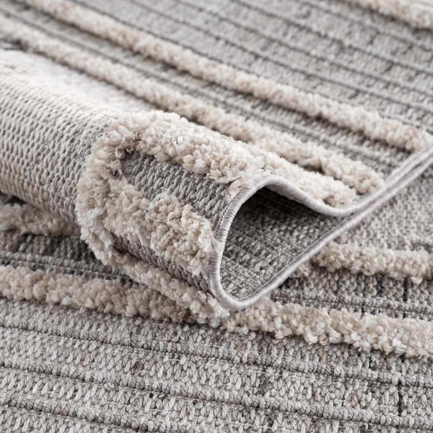 Close-up of the Amaga High-Low Rustic Rug, showing its charcoal, cream, and gray geometric pattern and textured, high-low pile. Fold