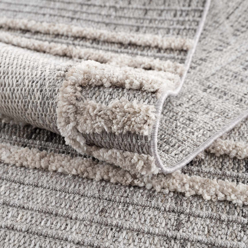 Close up of the Amaga High-Low Rustic Rug showing texture and pattern in cream, light beige, charcoal, and gray. Fold
