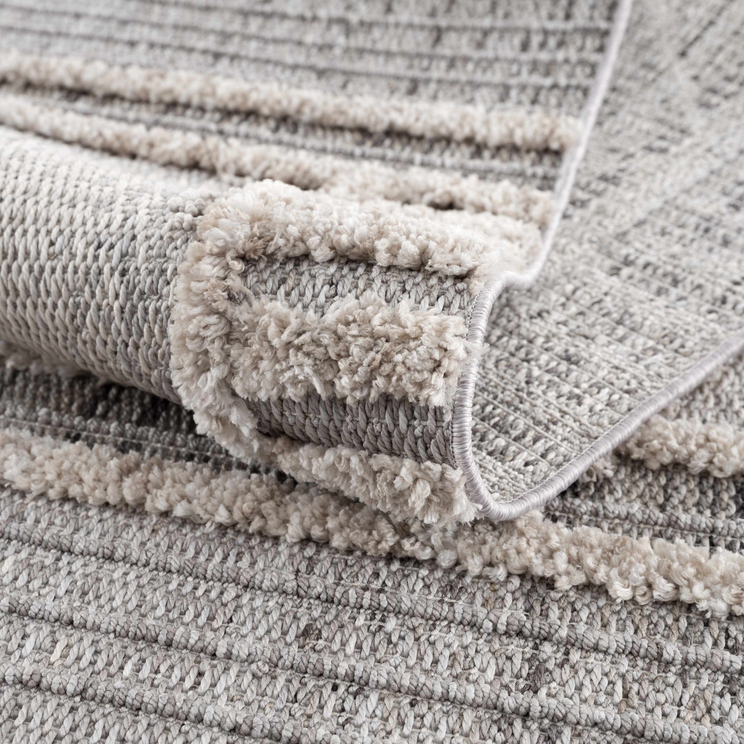 Close up of the Amaga High-Low Rustic Rug showing texture and pattern in cream, light beige, charcoal, and gray. Fold