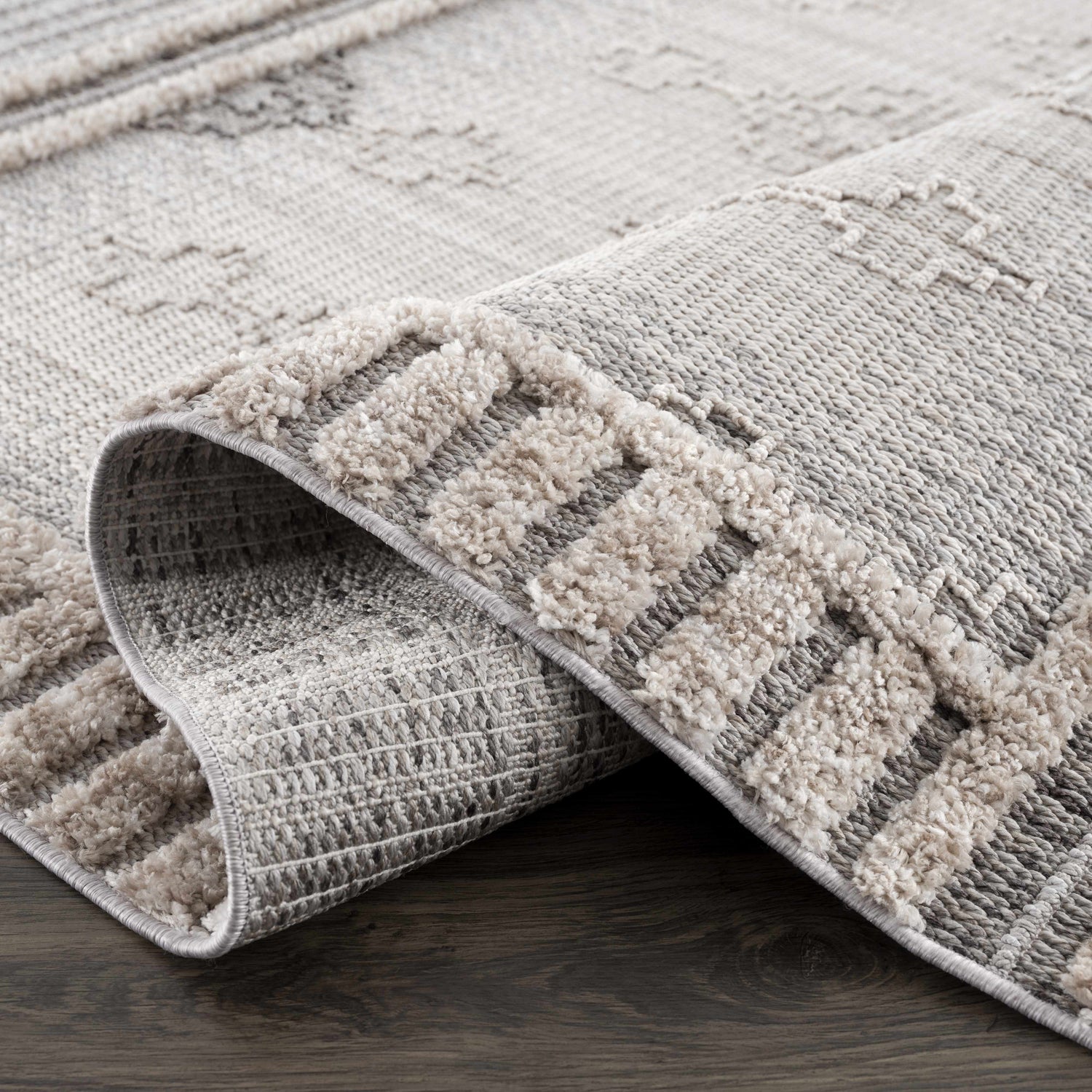 Close-up of the Amaga High-Low Rustic Rug showing its geometric pattern, charcoal, cream, and gray colors, and textured design. Fold