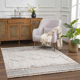 Living room scene with a cream Amaga High-Low Rustic Rug, light gray chair, wood cabinet, and plant. Roomscene-Rectangle