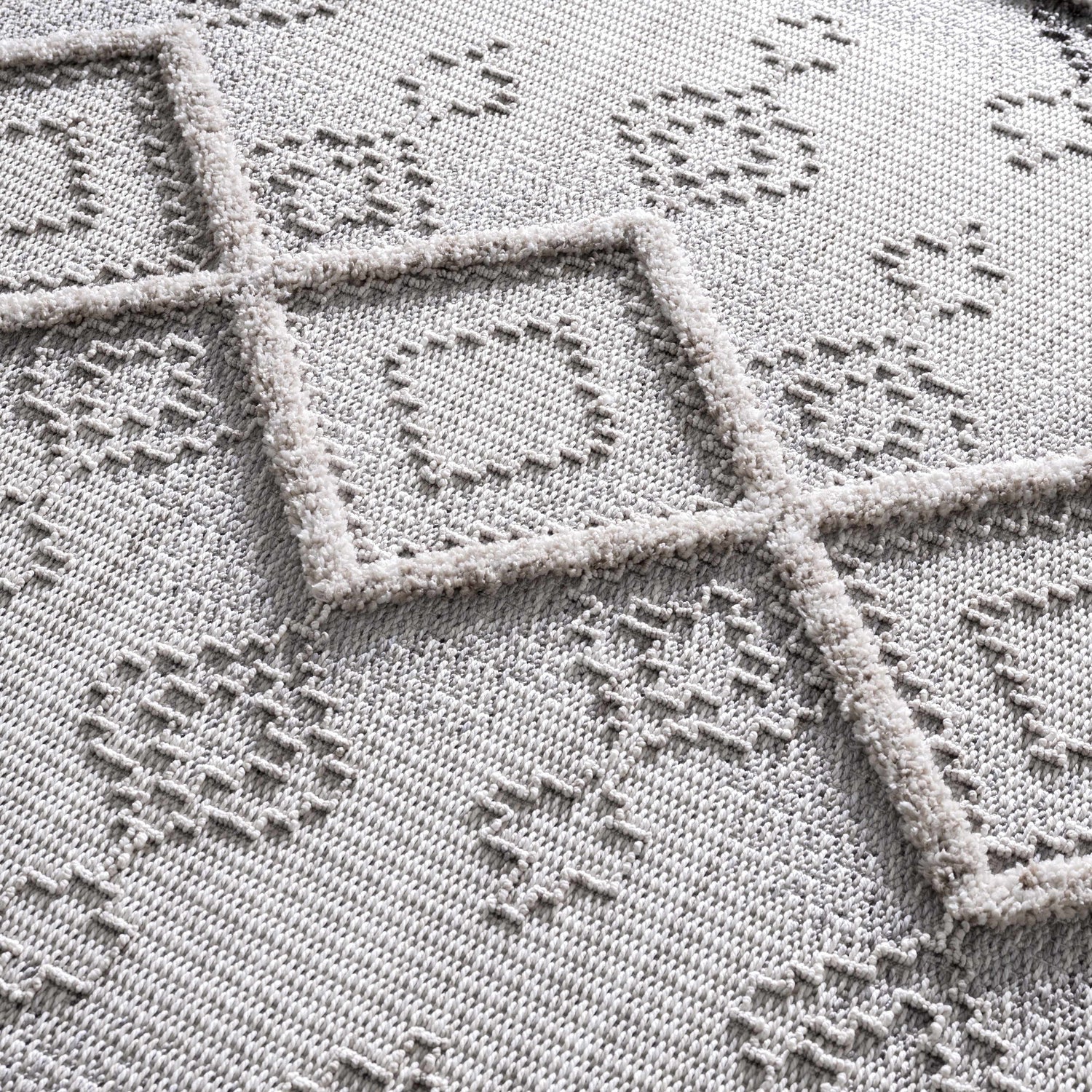 Close-up of the Amaga High-Low Rustic Rug showing its geometric pattern, high-low texture, and shades of gray and cream. Texture