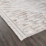 Close-up of the Poydras High-Low Rustic Rug, showcasing its beige, gray, and charcoal hues and textured, geometric design. Corner