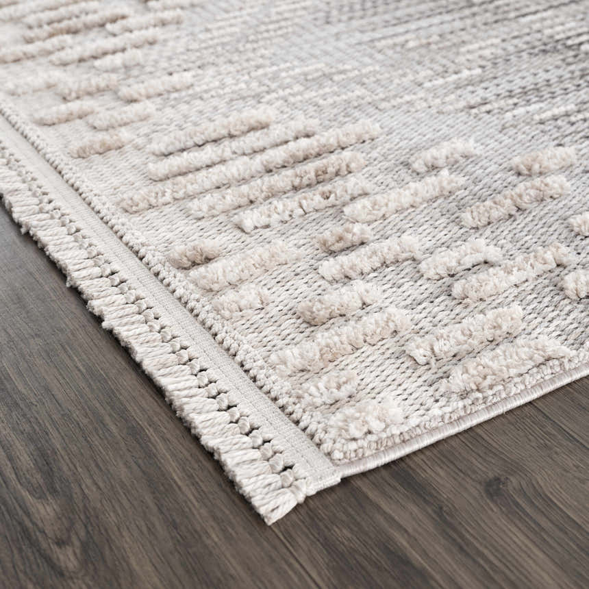 Close-up of the Poydras High-Low Rustic Rug, showcasing its beige, gray, and charcoal hues and textured, geometric design. Corner