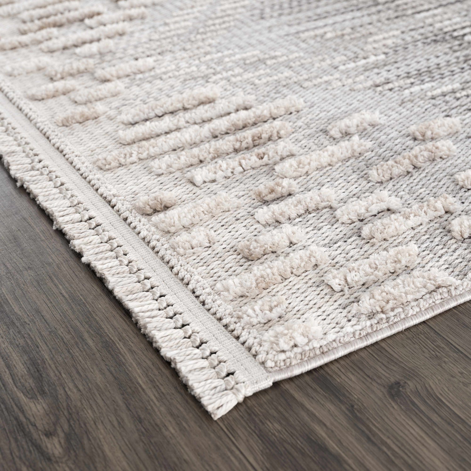 Close-up of the Poydras High-Low Rustic Rug, showcasing its beige, gray, and charcoal hues and textured, geometric design. Corner