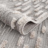Close up of the Poydras High-Low Rustic Rug showing its gray and beige textured design and machine-woven construction. Fold