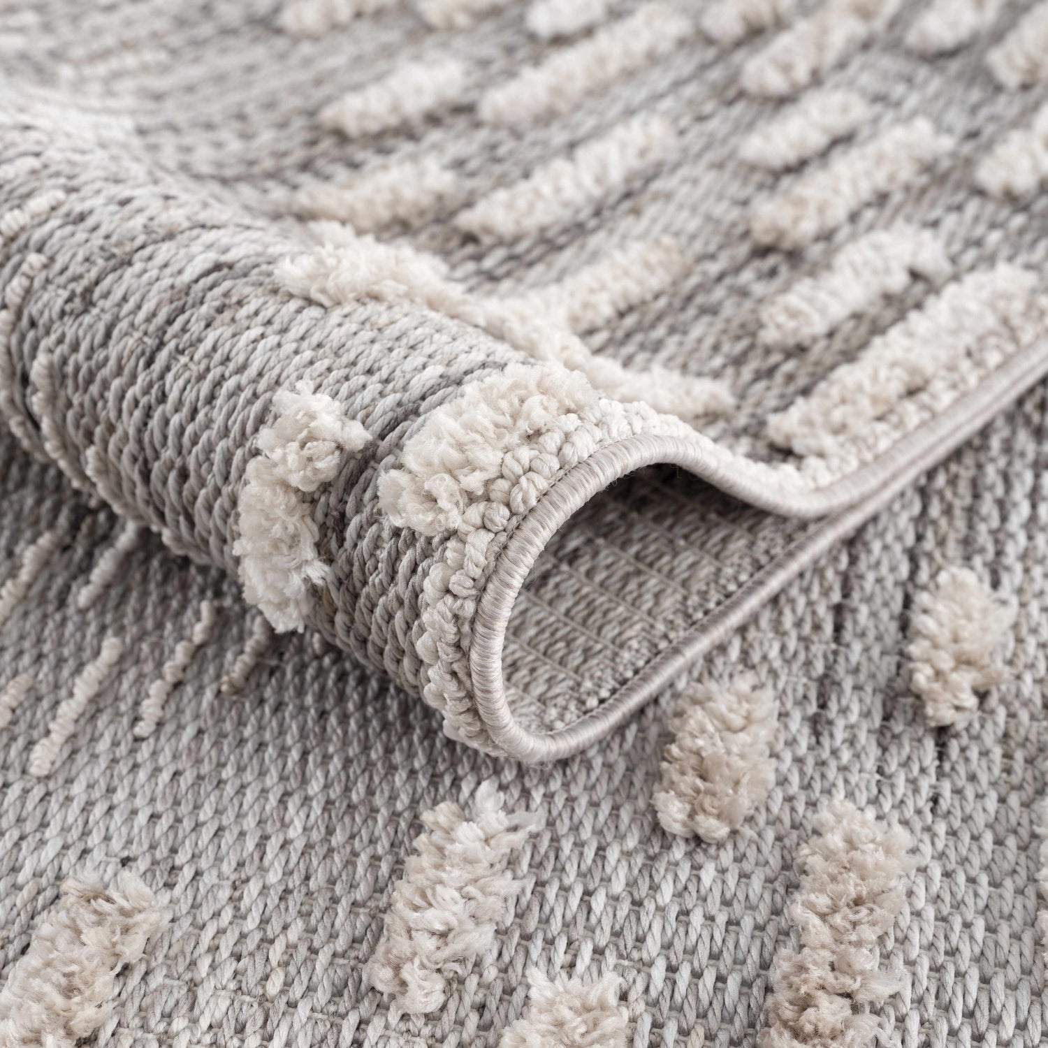 Close up of the Poydras High-Low Rustic Rug showing its gray and beige textured design and machine-woven construction. Fold
