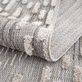Close-up of the Poydras High-Low Rustic Rug. Charcoal and gray rug with a textured, light beige geometric pattern. Fold
