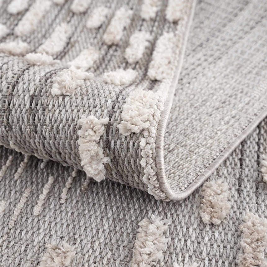 Close-up of the Poydras High-Low Rustic Rug. Charcoal and gray rug with a textured, light beige geometric pattern. Fold