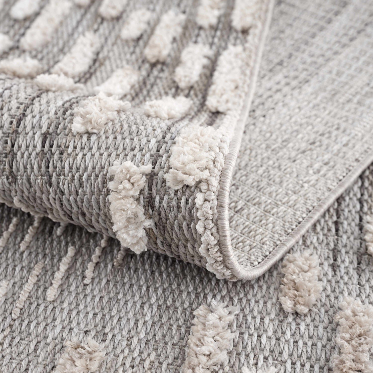 Close-up of the Poydras High-Low Rustic Rug. Charcoal and gray rug with a textured, light beige geometric pattern. Fold