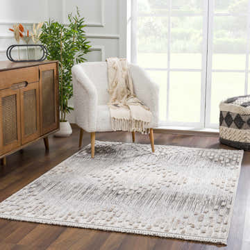 Living room scene with a Poydras High-Low Rustic Rug in charcoal, gray, and beige, styled with a white chair and wood cabinet. Roomscene-Rectangle