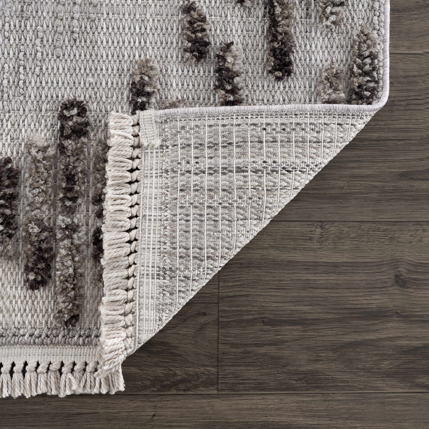 Close-up of the Cabarroguis Area Rug showing the charcoal geometric pattern, cream fringe, and woven texture. Fold