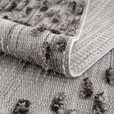 Close up of the Cabarroguis Area Rug showing charcoal geometric pattern and textured cream weave. Fold