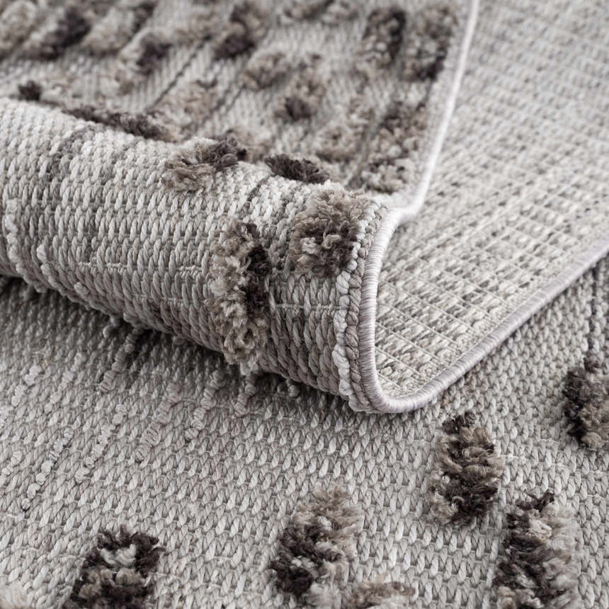 Close up of the Cabarroguis Area Rug showing charcoal geometric pattern and textured cream weave. Fold