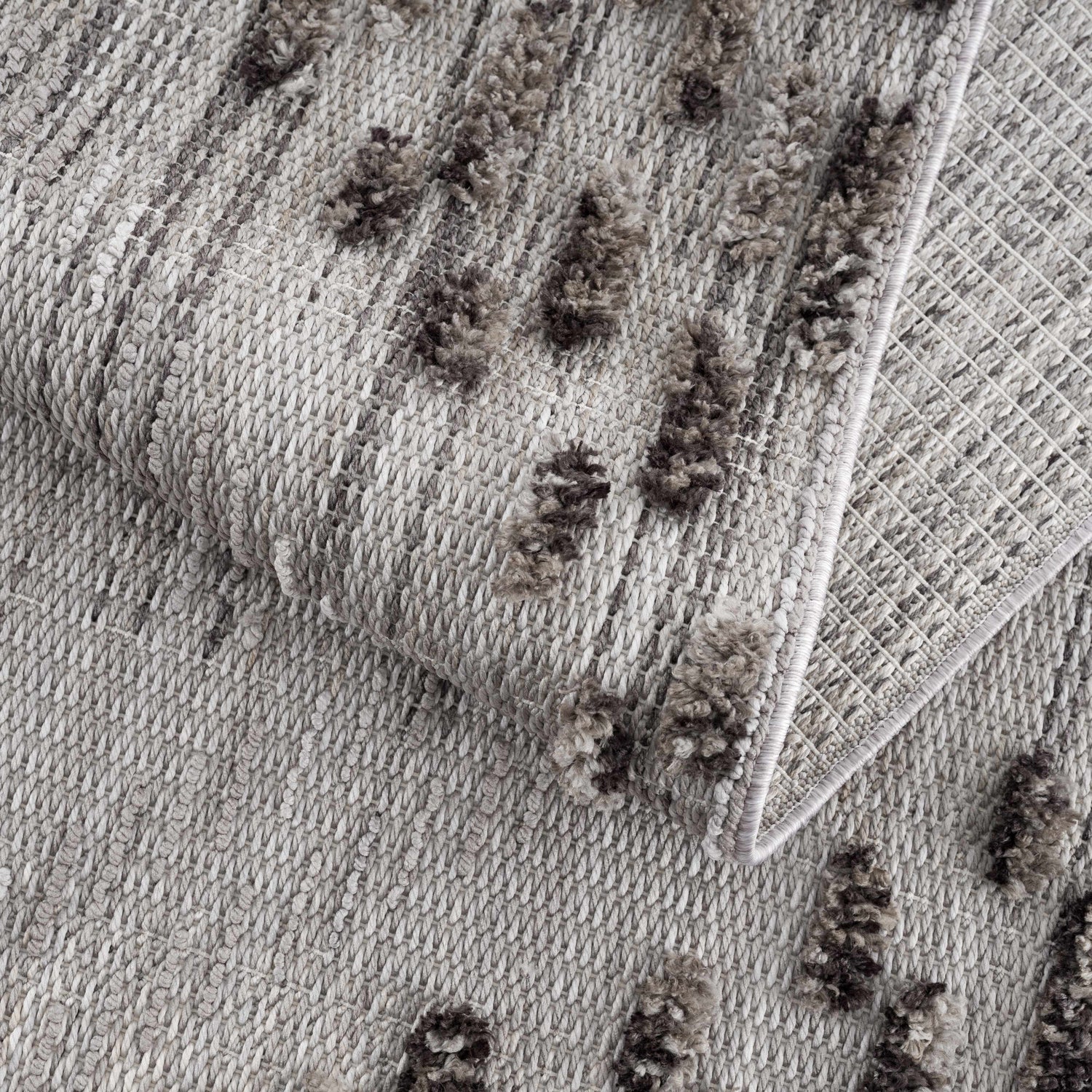 Close-up of the Cabarroguis Area Rug showing its charcoal and cream geometric pattern and textured, machine-woven construction. Fold