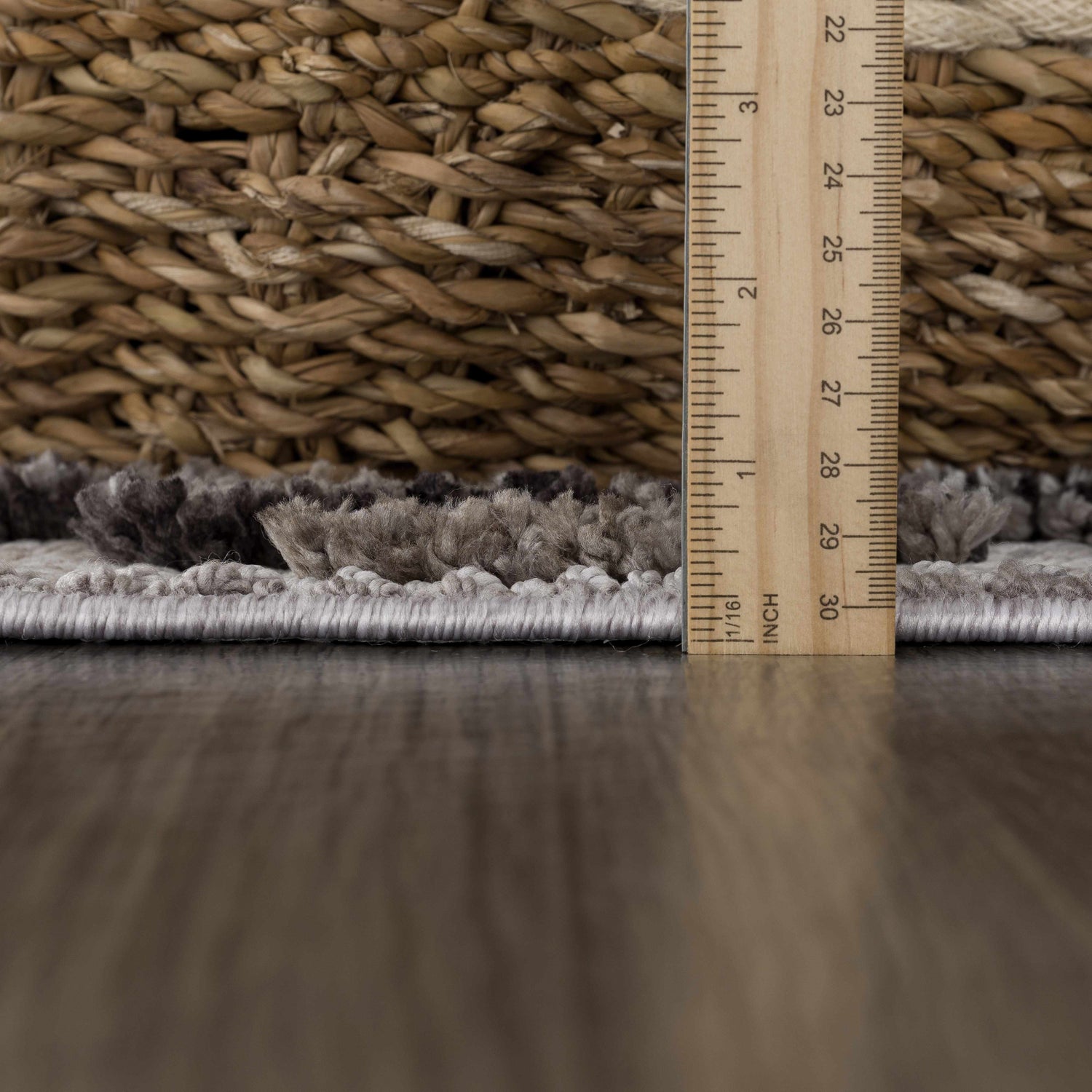 Close-up of the plush texture of the Cabarroguis Area Rug in charcoal, cream, and gray with a ruler for pile height. Pile