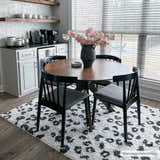 Dining room with round wood table on Zhen Black Spots Leopard Rug. Modern black chairs, white cabinets, and pink flowers. Roomscene-Rectangle