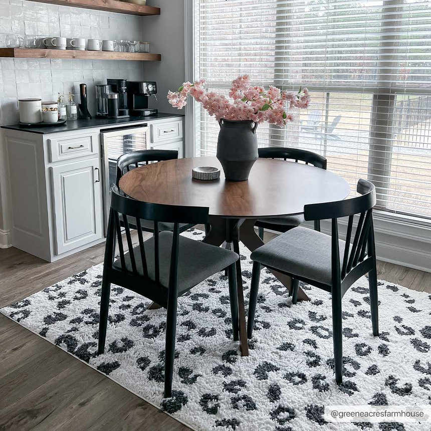 Dining room with round wood table on Zhen Black Spots Leopard Rug. Modern black chairs, white cabinets, and pink flowers. Roomscene-Rectangle