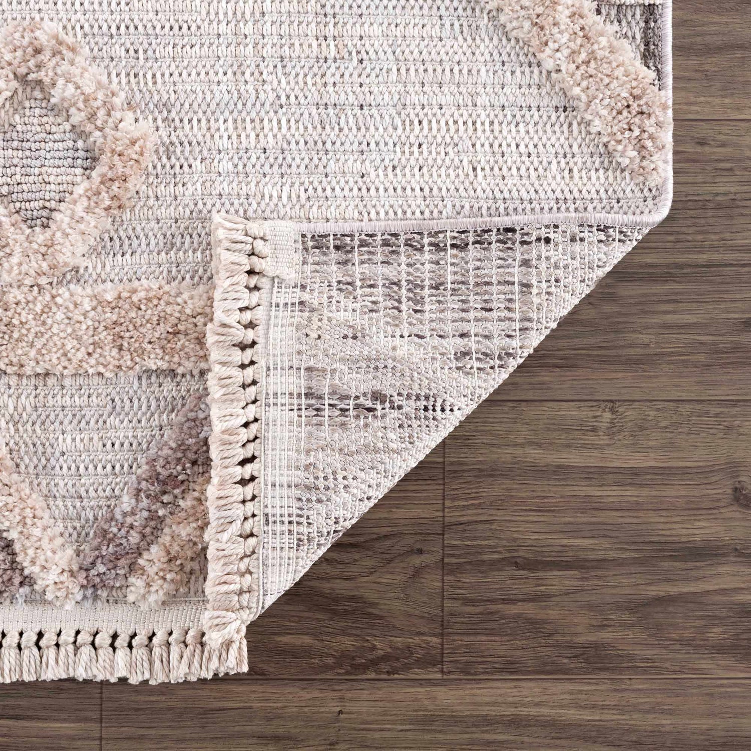Close-up of the Serkomen High-Low Area Rug showing its woven texture, geometric pattern, and fringe detail on wood floor. Fold