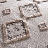 Close-up of Serkomen High-Low Area Rug. Beige polyester rug with geometric square pattern and textured, high-pile details. Texture