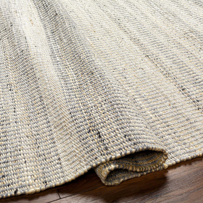 Close-up of the hand woven Abucay Jute Rug, showcasing its charcoal, cream, and light beige colors and textured weave. Fold