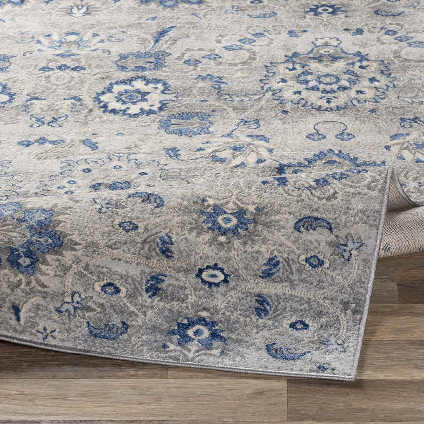 Close-up of the Adairsville Blue Floral Area Carpet, featuring a denim and gray traditional floral pattern. Fold