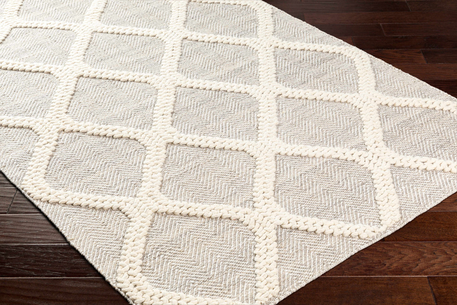 Close-up of the Adora Area Rug in bone and cloud gray, featuring a geometric diamond pattern with braided accents. Corner