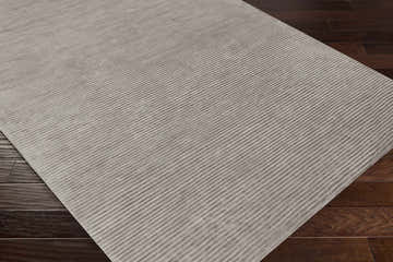 Close-up of the hand-loomed Ahmeek Area Rug in medium gray viscose, featuring a subtle striped texture on a dark wood floor. Corner