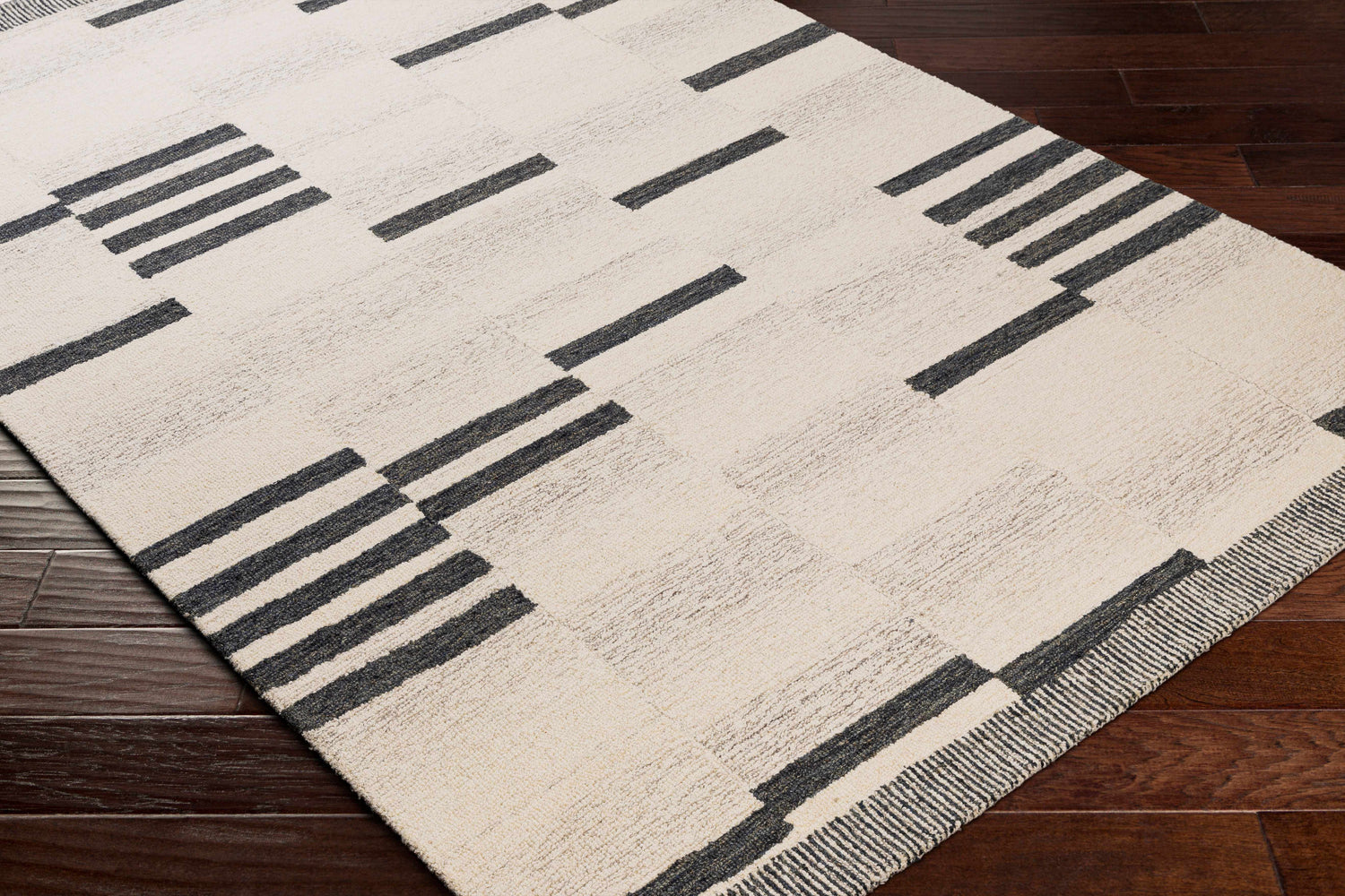 Close up of Aibonito Hand Tufted Wool Area Rug. Beige rug with black geometric stripes on a dark wood floor. Corner