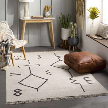 Living room scene with Aisha area rug, geometric pattern, neutral tones, leather pouf, and modern decor. Roomscene-Rectangle