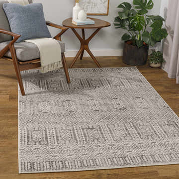 Living room scene with gray Akdiken Area Carpet, wood chair with blue pillow, side table, and monstera plant. Roomscene-Rectangle