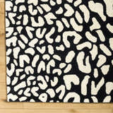 Close-up of the Akeem Leopard Print Area Rug. Black and beige wool rug with a contemporary animal print pattern. Corner