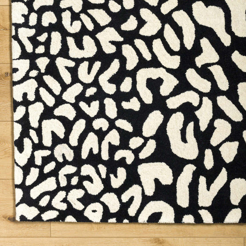 Close-up of the Akeem Leopard Print Area Rug. Black and beige wool rug with a contemporary animal print pattern. Corner