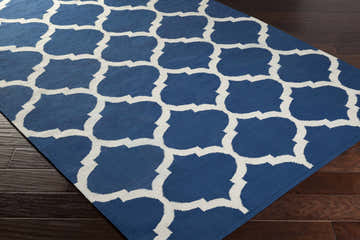 Close-up of the Alcalde Area Carpet on dark wood floors. Features a bright blue and ivory quatrefoil pattern. Hand woven cotton rug. Corner